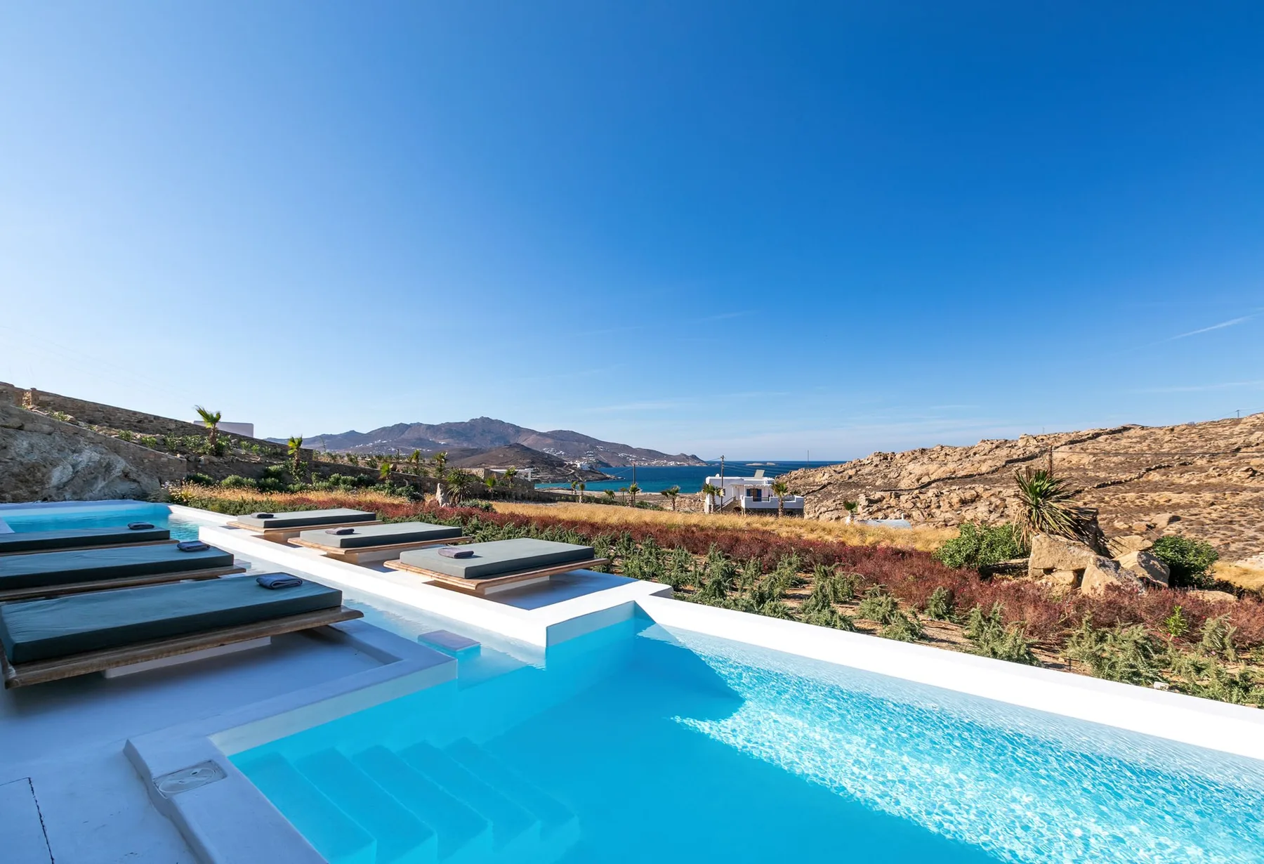 Una piscina con asientos sumergidos ofrece vistas a una ladera árida y al mar.