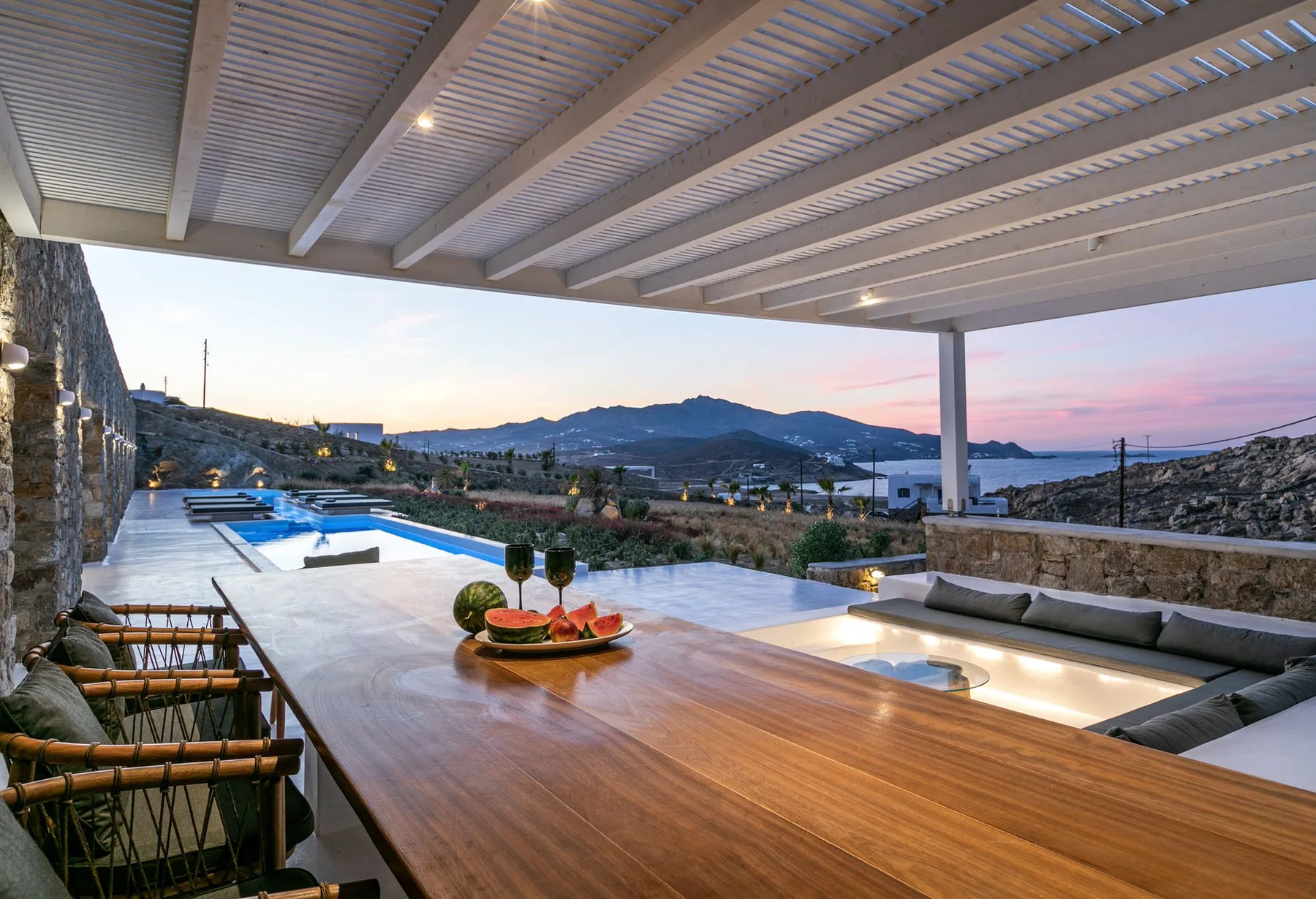 A covered outdoor patio overlooks a pool and distant hills at dusk.