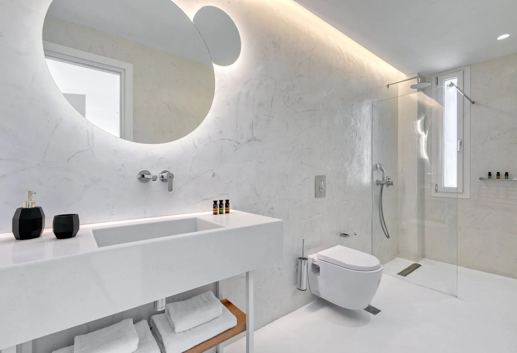 A bright bathroom with a wide sink, wall-mounted toilet, and glass shower.