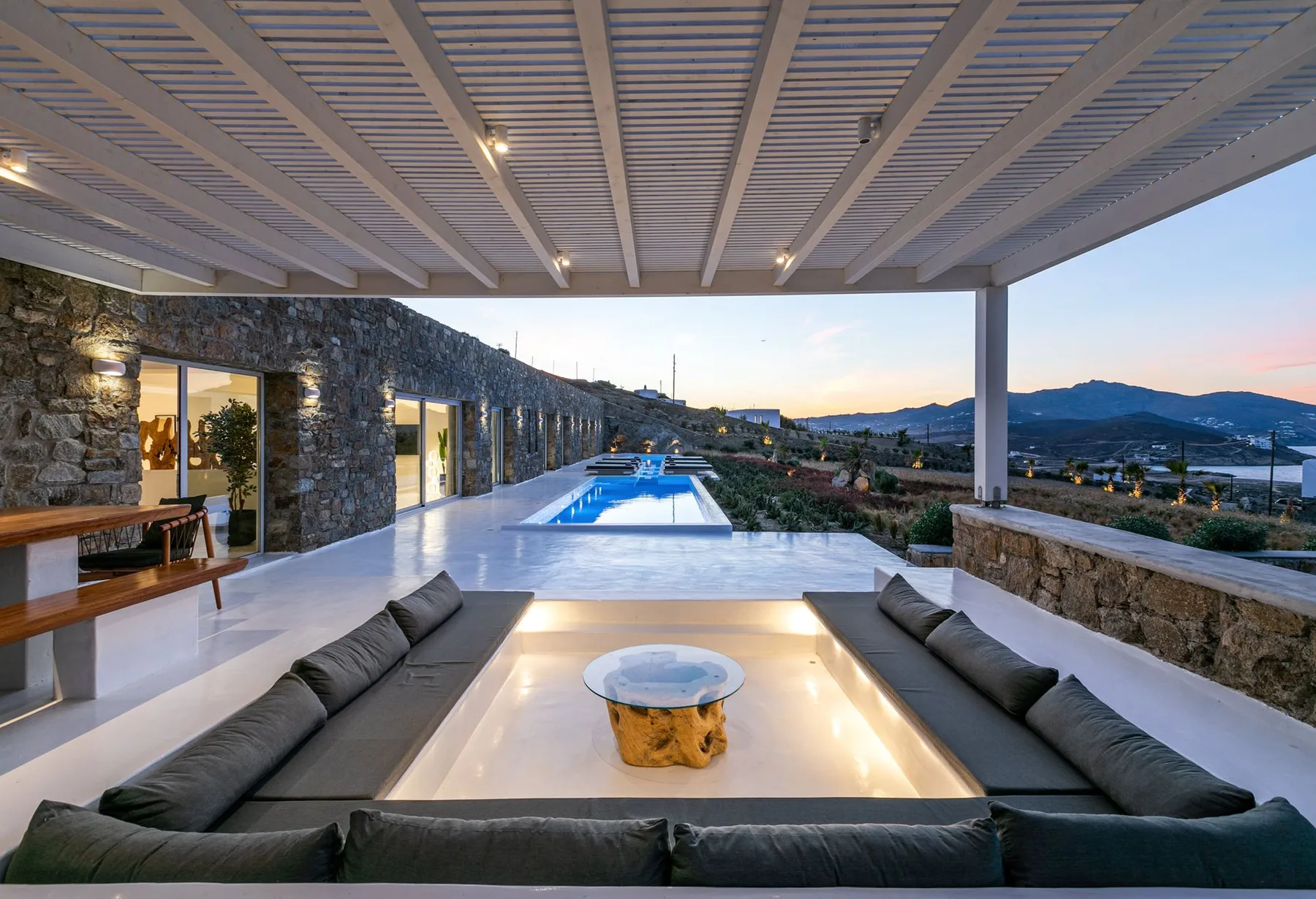 Una sala exterior cubierta da a una piscina y colinas lejanas.