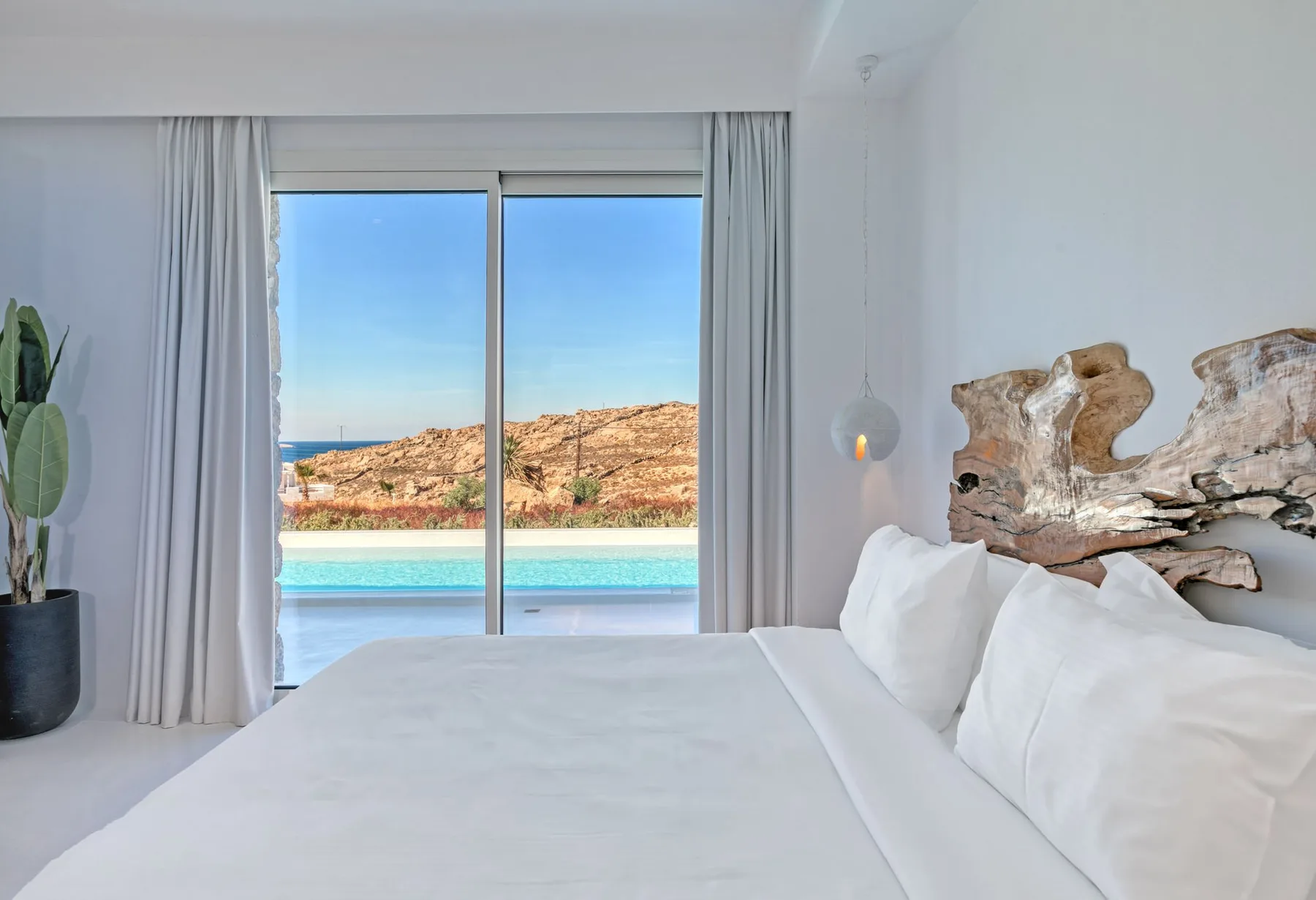 A bright bedroom with a white bed facing a window overlooking a pool.