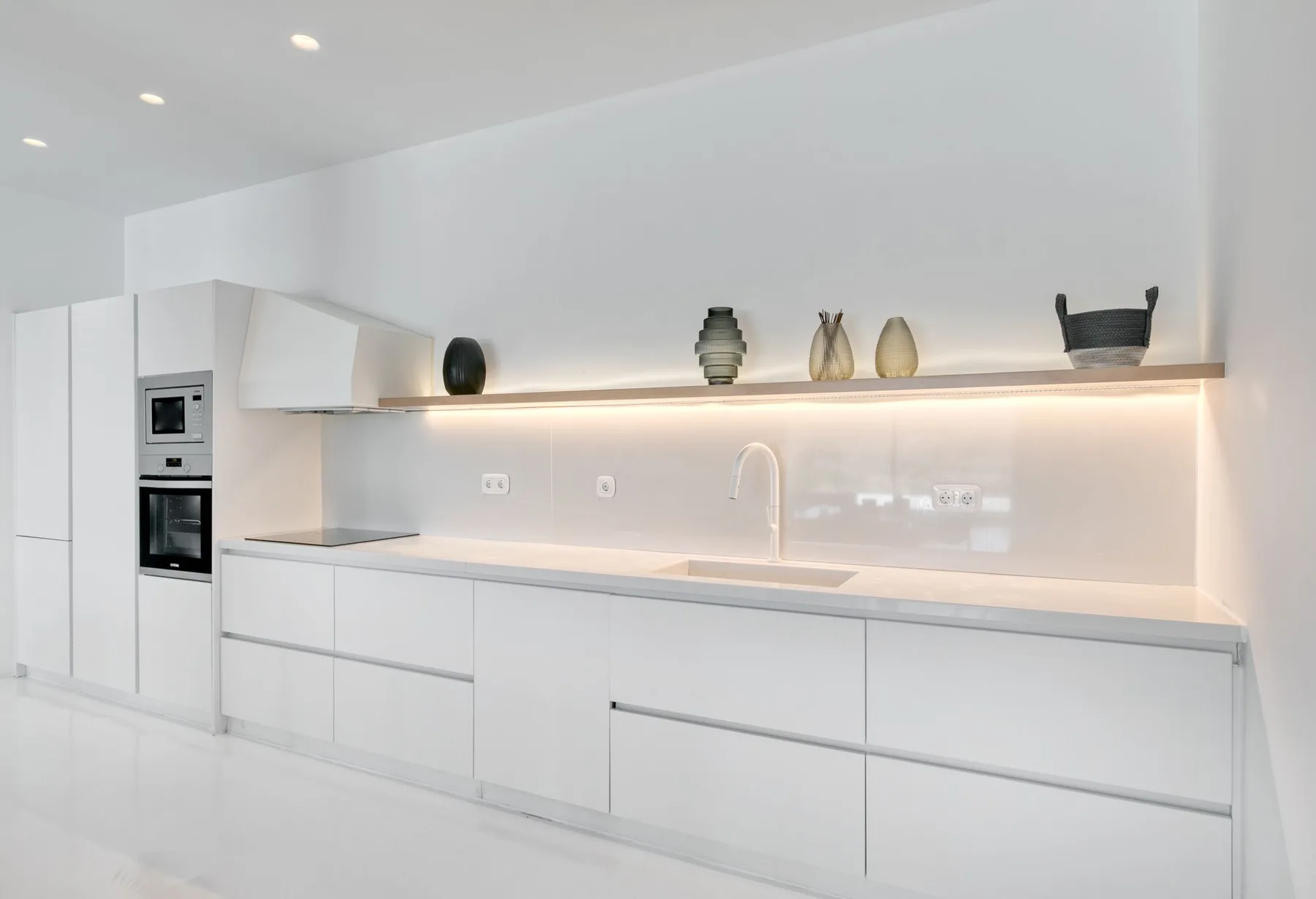 Una cocina moderna blanca con una encimera larga y electrodomésticos integrados.