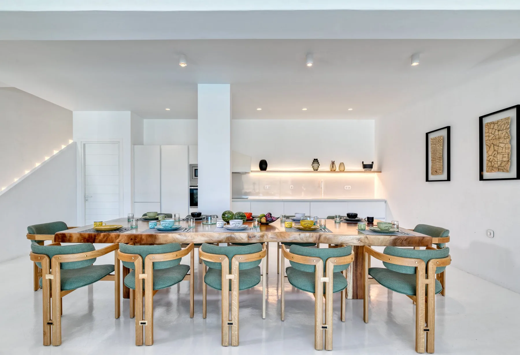A bright dining area with a long table and teal seating.