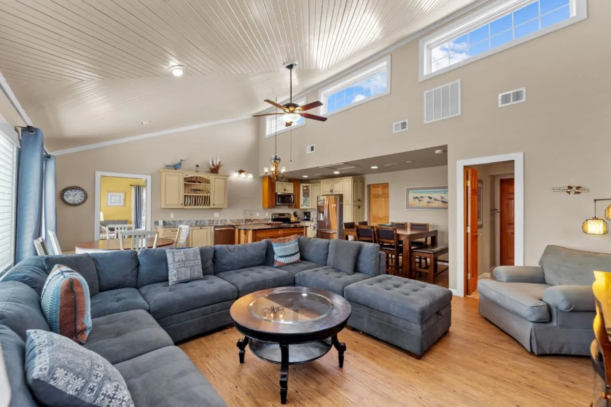 A spacious living area with sectional seating, a coffee table, and a kitchen in the background.