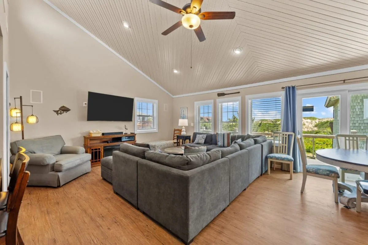 A bright living room with ample seating, a television, and sliding glass doors.