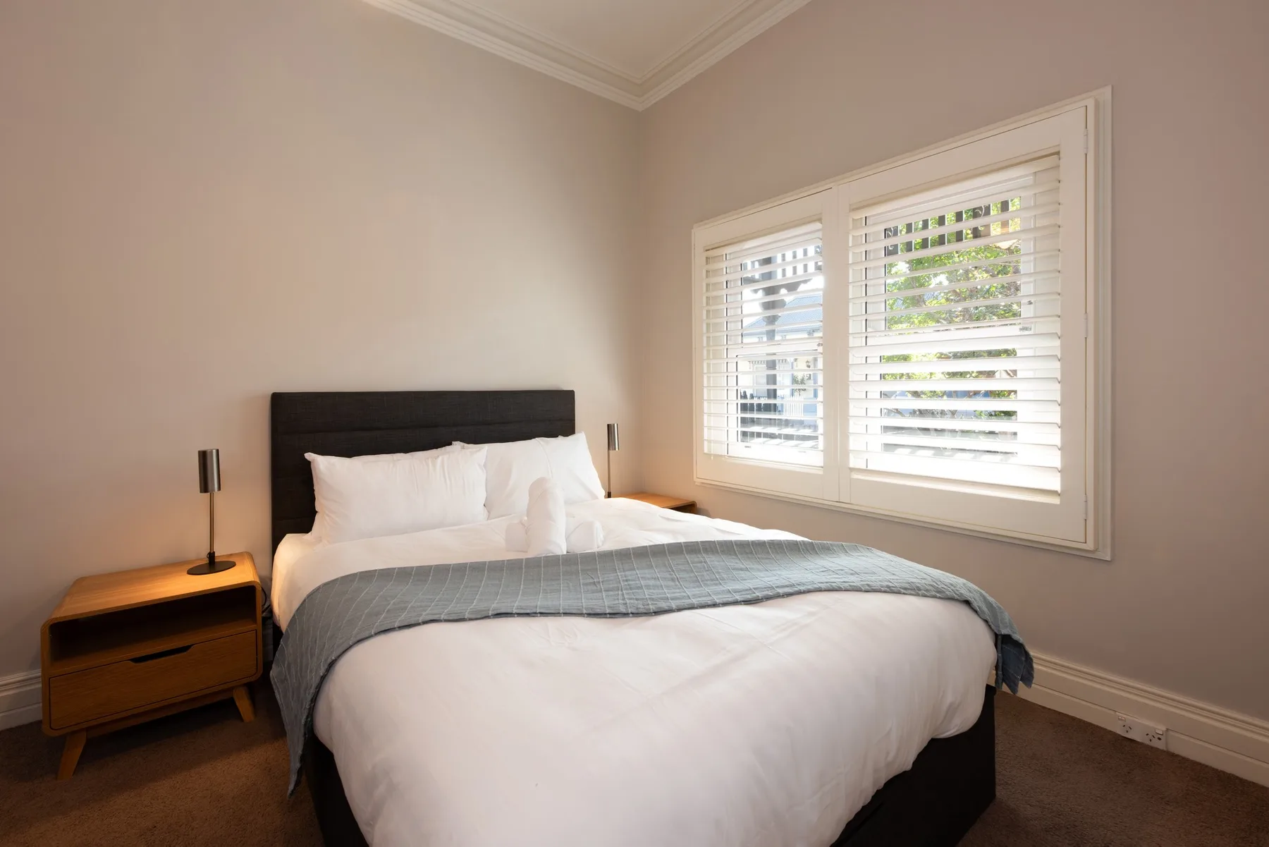 A bedroom with a neatly made bed and a wide shuttered window.