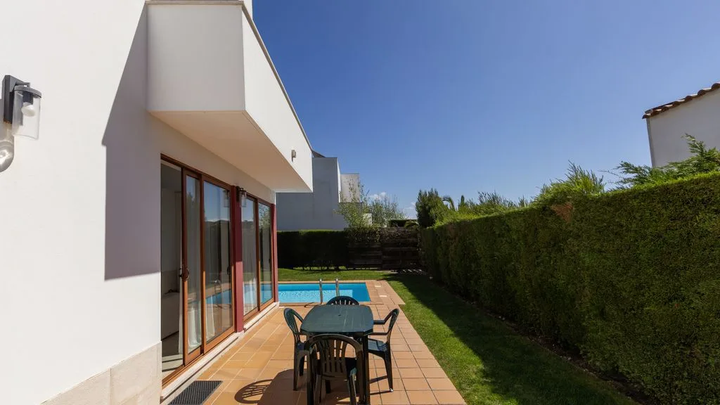 Un patio soleado junto a una casa moderna da a una piscina pequeña.