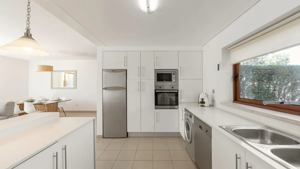 Una cocina luminosa con armarios blancos y electrodomésticos de acero inoxidable.