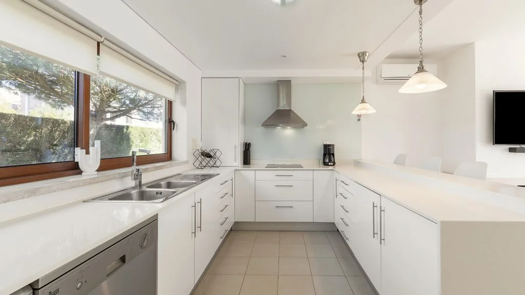 Una cocina blanca y luminosa con una campana extractora y ventanales.