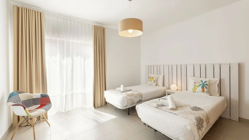 Un dormitorio luminoso con dos camas y una gran ventana con cortinas.