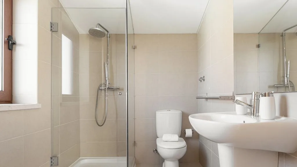 Un baño luminoso con ducha de vidrio, inodoro y lavabo.