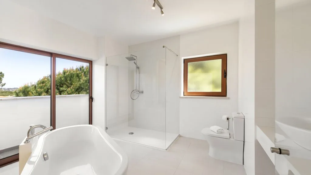 Un baño luminoso cuenta con bañera, ducha de cristal y ventanas amplias.