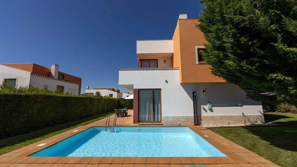 Una villa moderna se encuentra junto a una piscina rectangular y un jardín.