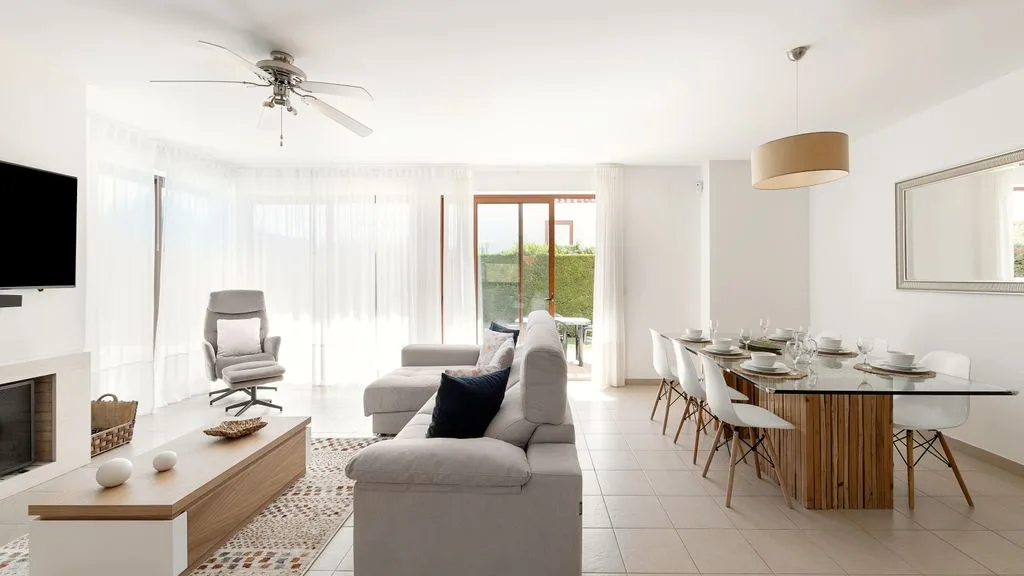 Un luminoso salón-comedor con un sofá seccional y una mesa de comedor de vidrio.