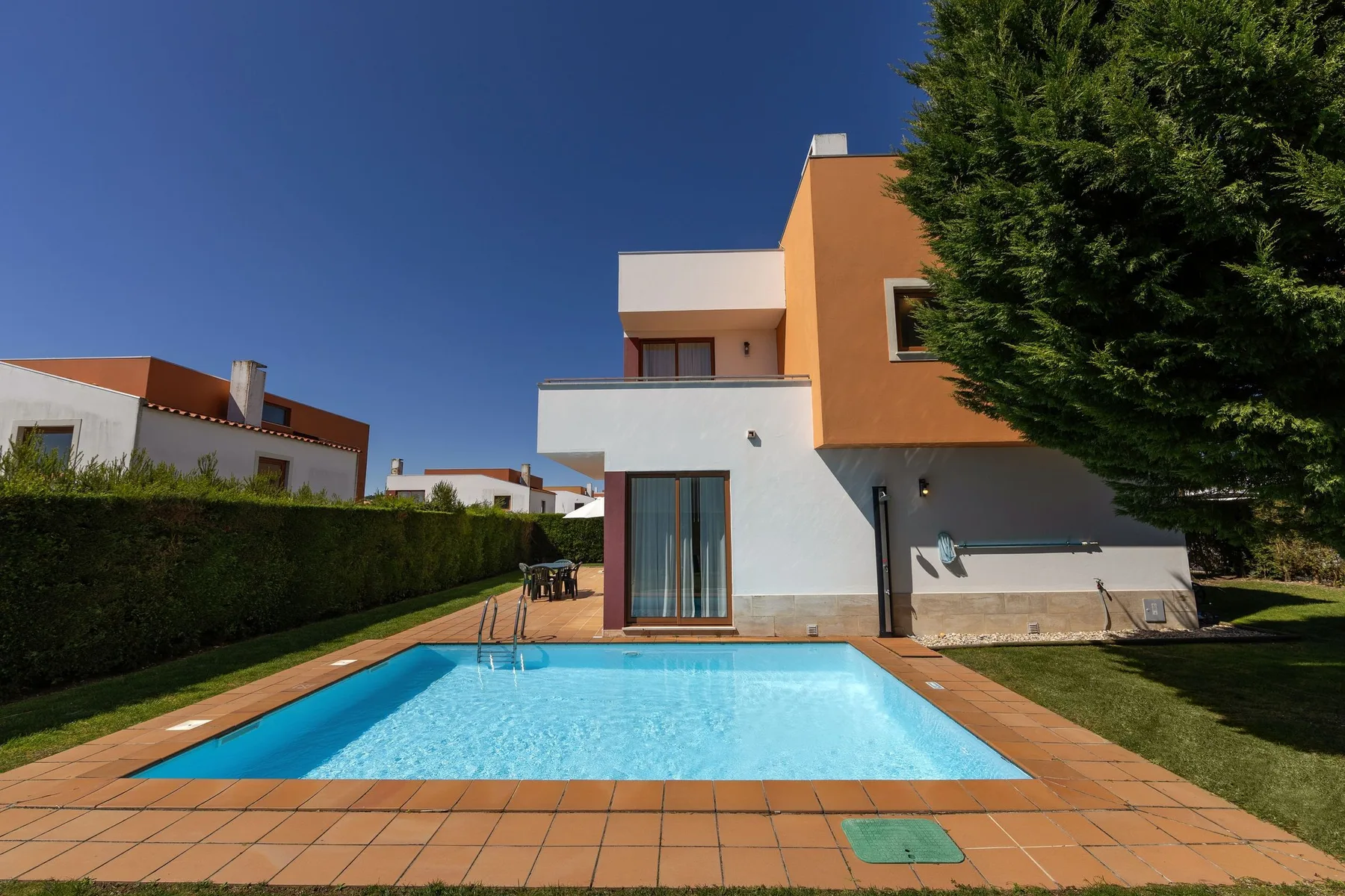 A swimming pool beside a modern house and landscaped yard.