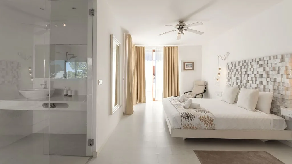 A bright bedroom with a bed, a seating area, and a glass-enclosed shower.