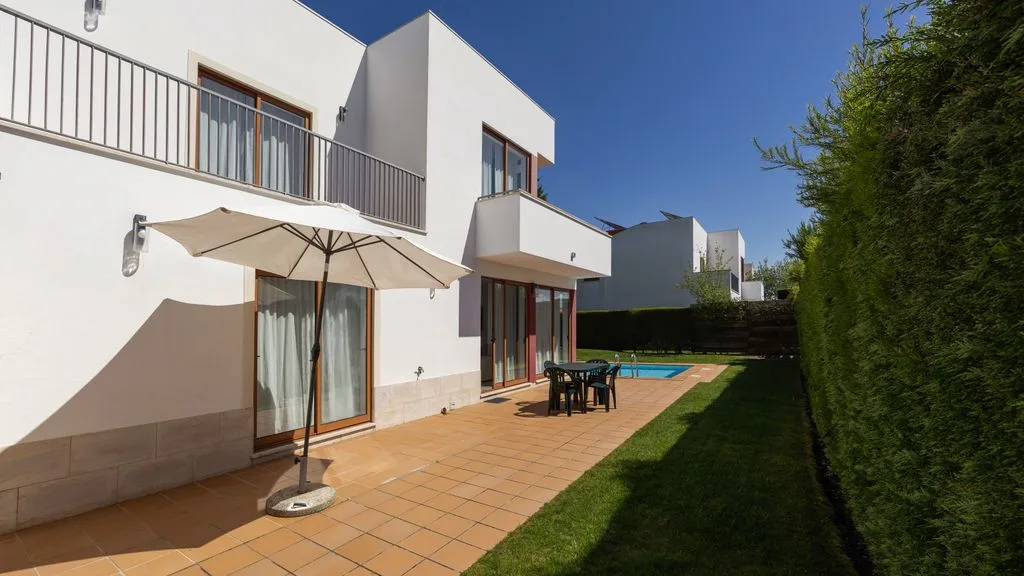 Patio de una villa moderna con sombrilla, asientos al aire libre y piscina.