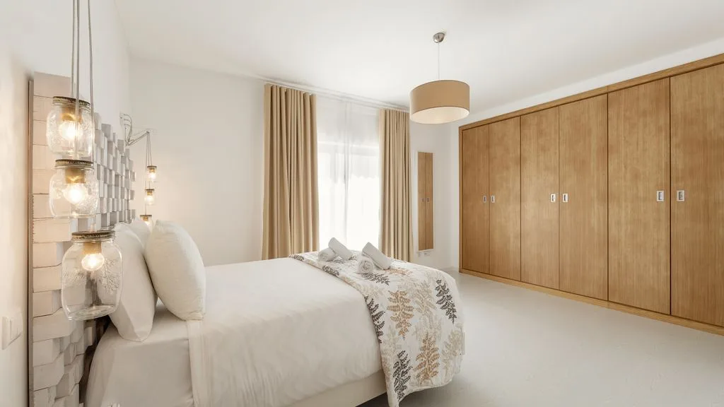 Un dormitorio luminoso con una cama, ropa de cama estampada y armarios de madera.