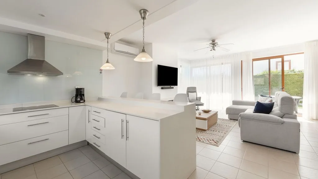 Una cocina abierta al salón con muebles blancos y zona de estar.