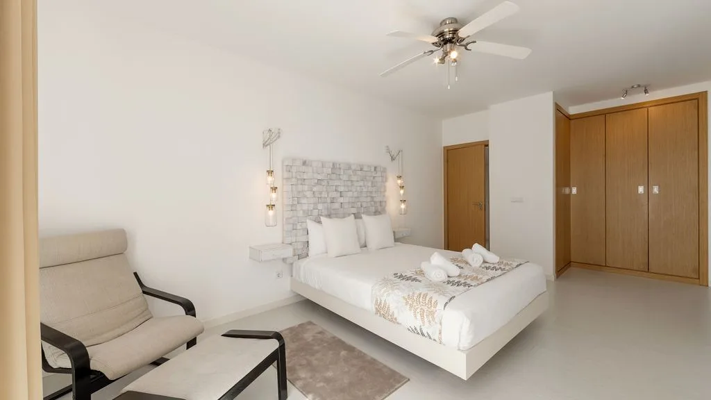Un dormitorio con una cama, luces junto a la cama y un ventilador de techo.