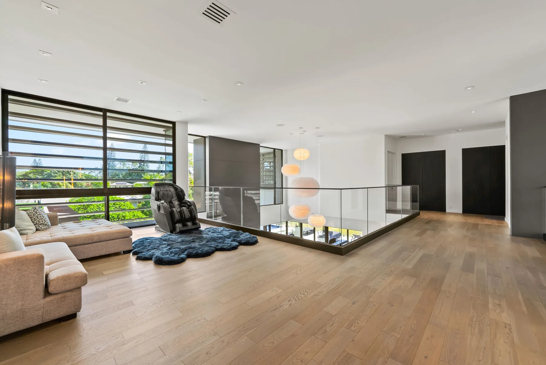 Una amplia sala de estar con grandes ventanas, asientos y una barandilla de vidrio alrededor de la escalera.