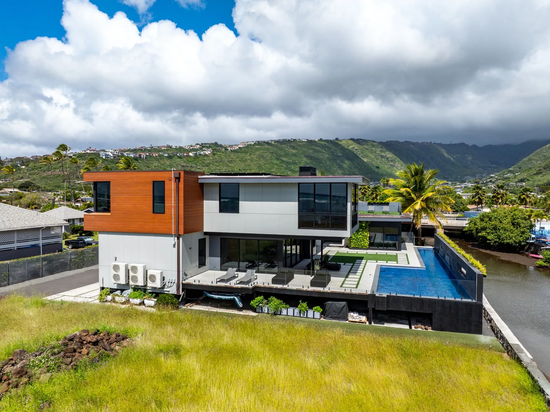Una casa moderna con piscina está rodeada de colinas verdes bajo un cielo nublado.