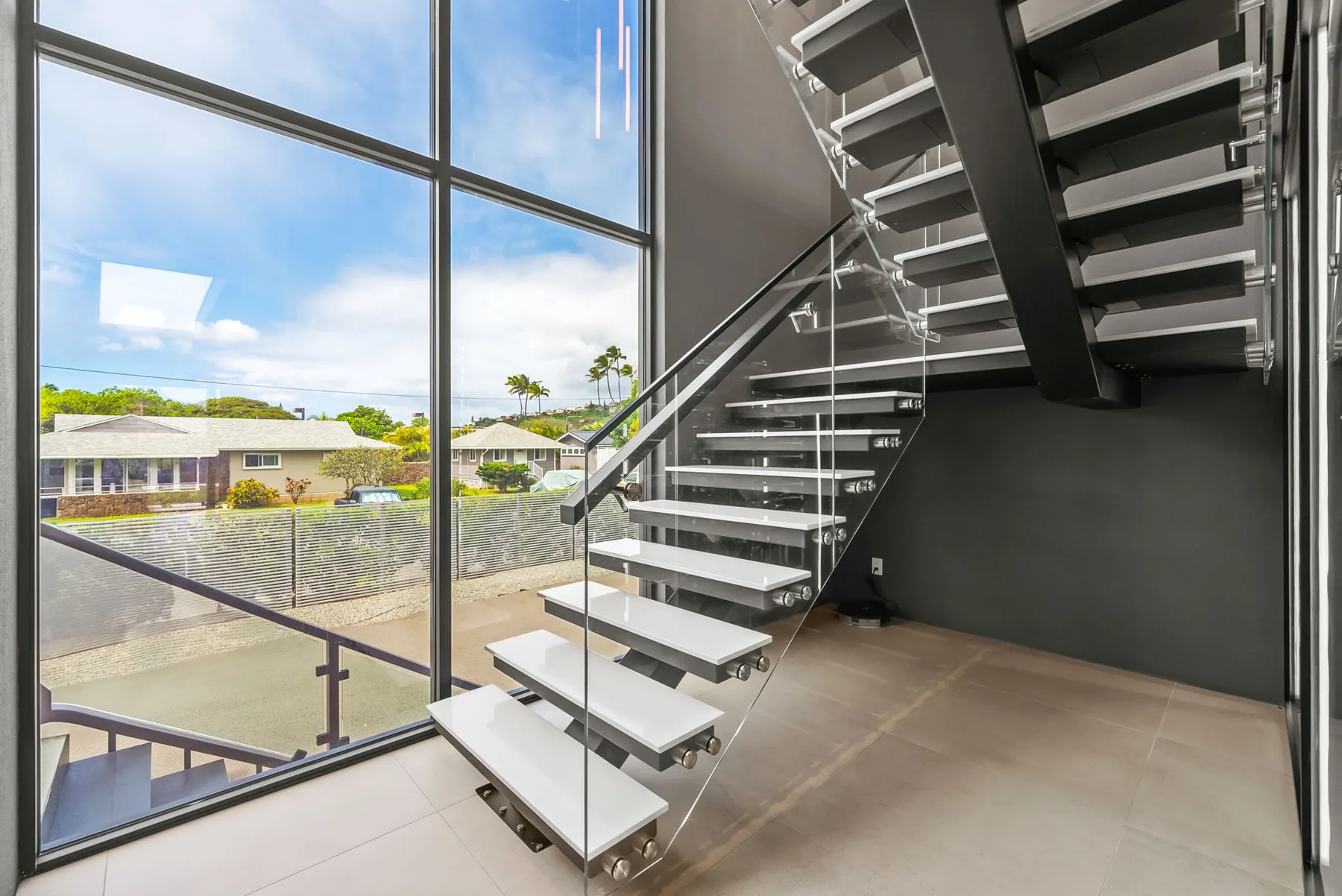 Una escalera interior moderna con peldaños abiertos junto a una gran pared de vidrio.