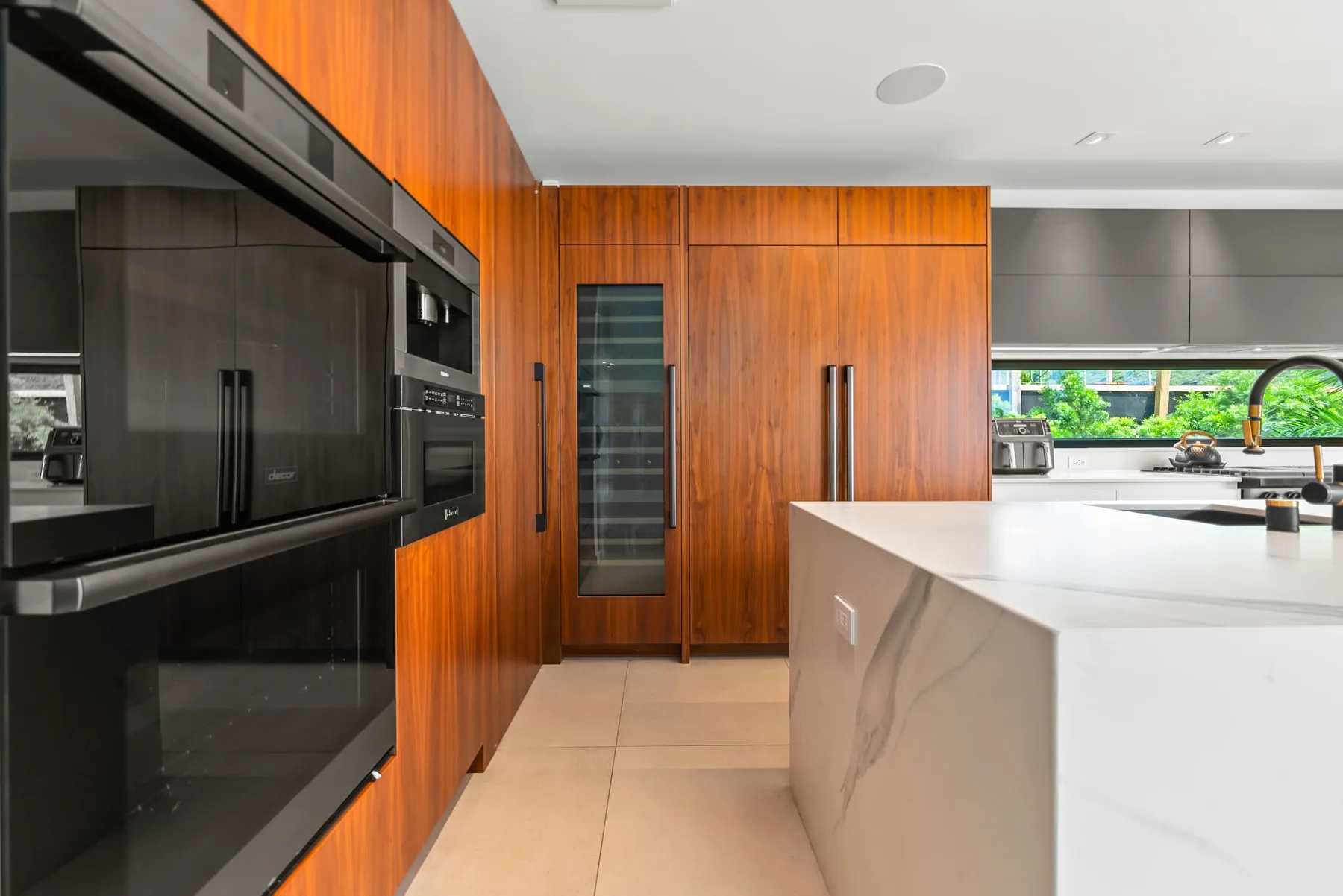 Una cocina moderna con gabinetes de madera, electrodomésticos oscuros y una isla blanca.