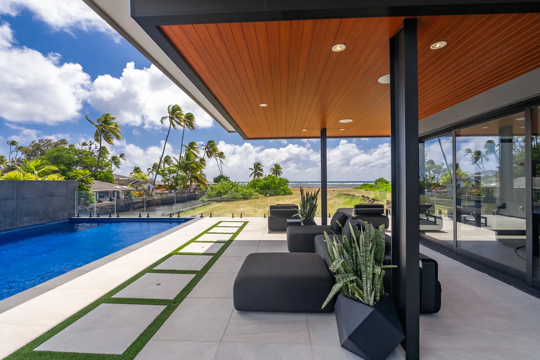 Un patio cubierto junto a una piscina, con asientos al aire libre y puertas de vidrio.
