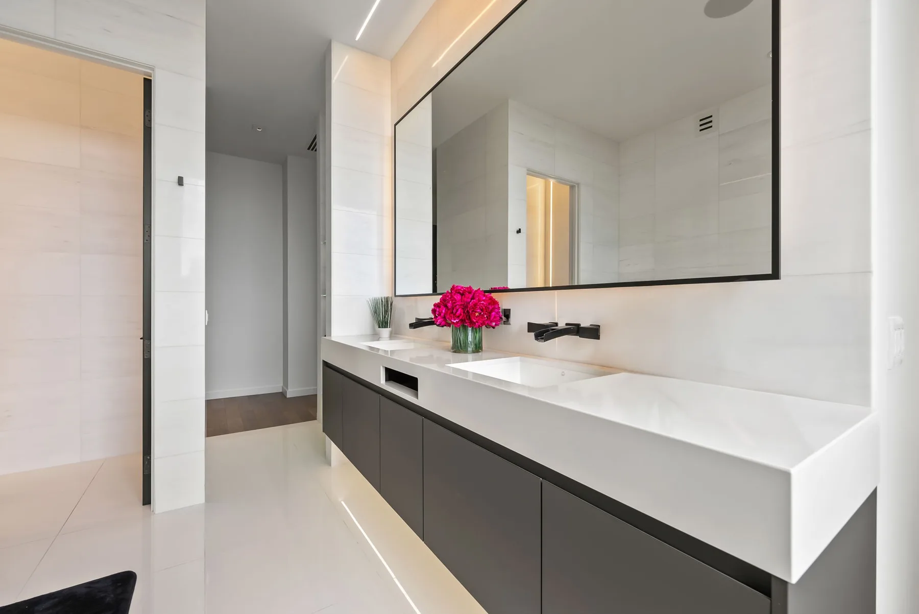 Un baño moderno con un largo tocador, un espejo grande y flores.
