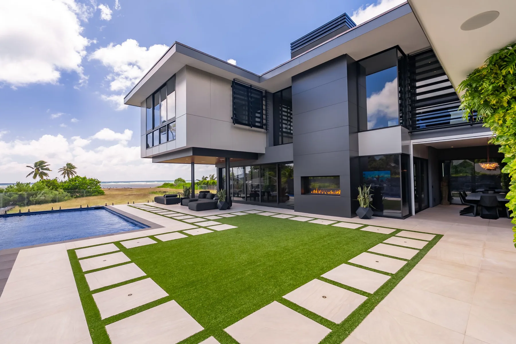 Una casa moderna se abre a un patio ajardinado con piscina y asientos al aire libre.