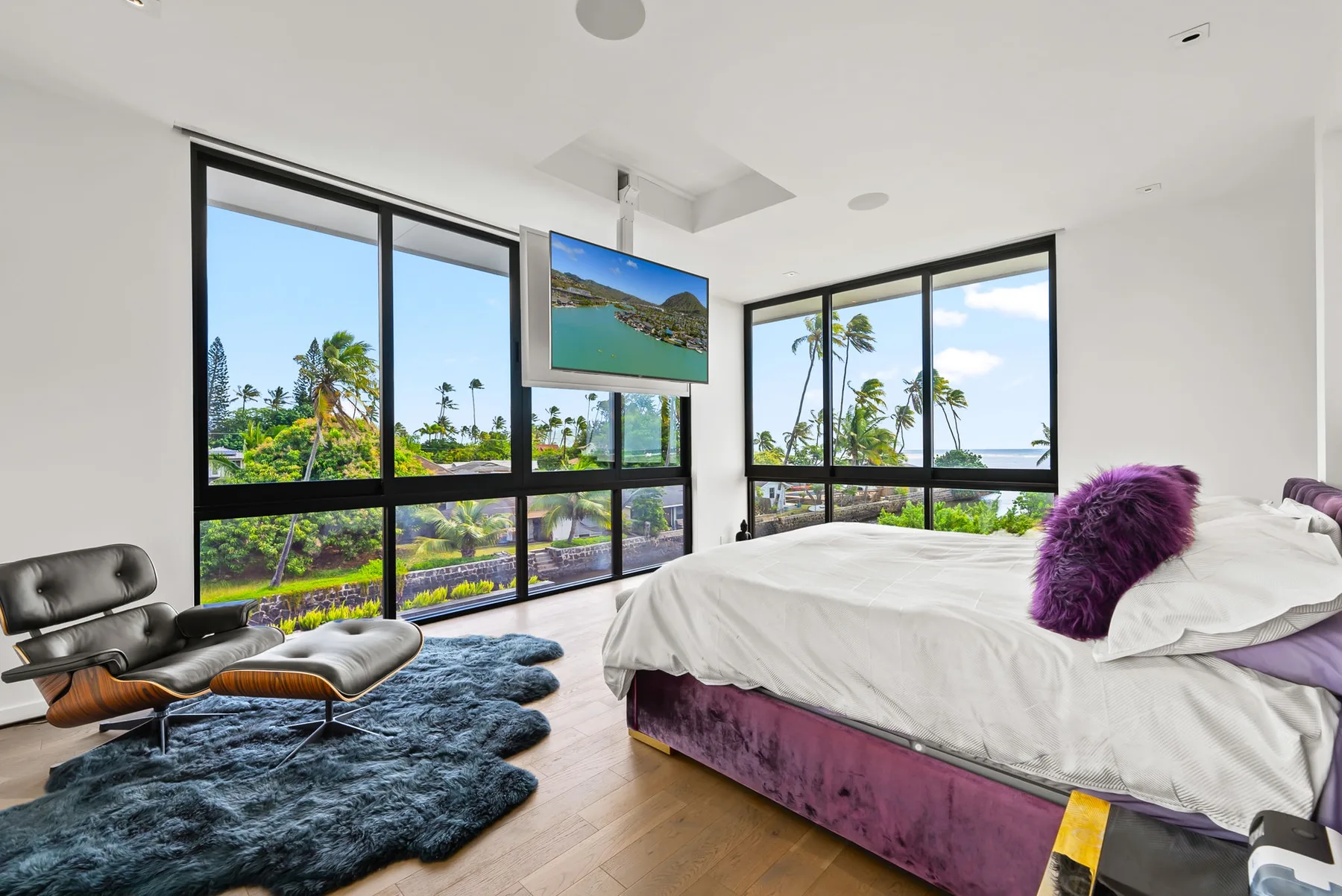 Un dormitorio con cama, asientos de descanso y grandes ventanas con vista a palmeras.