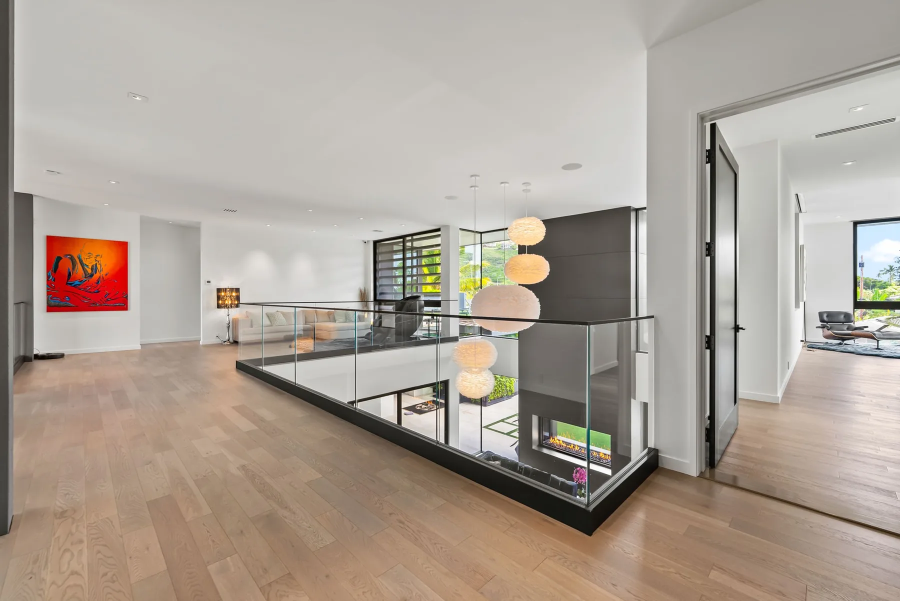 Un pasillo superior luminoso da a un espacio interior con barandilla de vidrio.