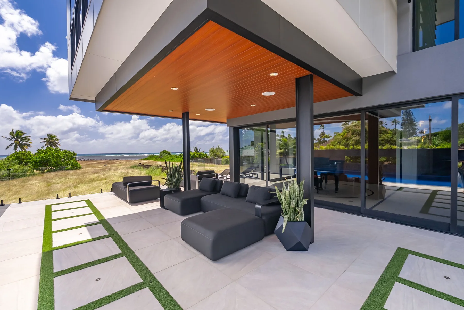 Un patio de una casa moderna con asientos al aire libre bajo un alero revestido de madera.