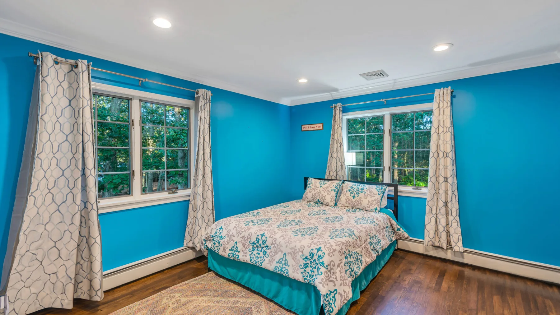 A bedroom with a bed between two windows and bright blue walls.
