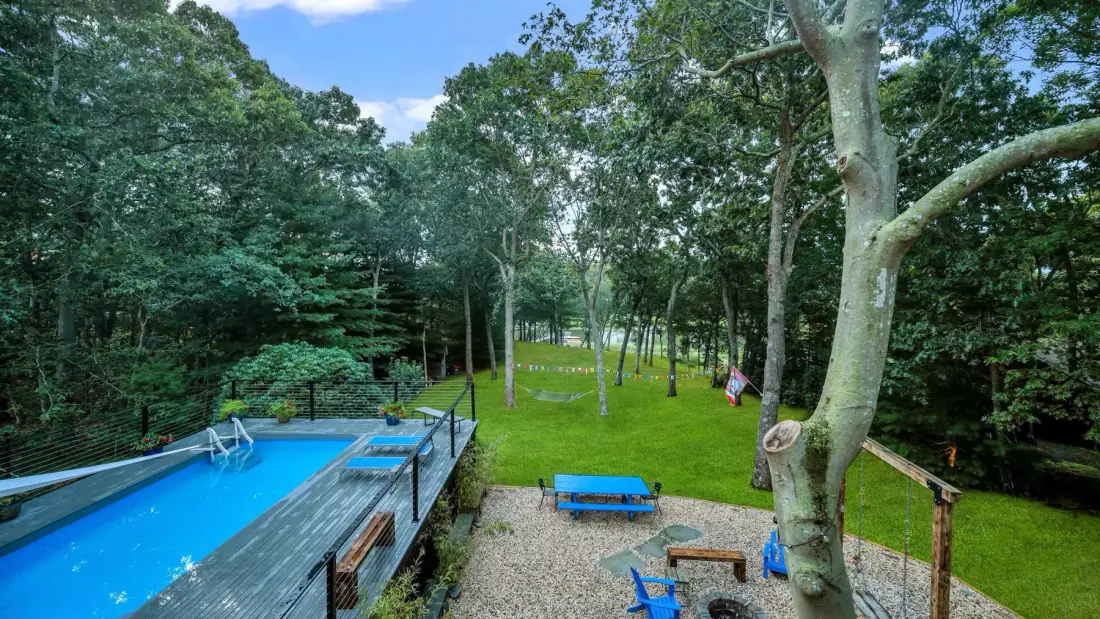 An outdoor swimming pool borders a grassy clearing surrounded by trees.