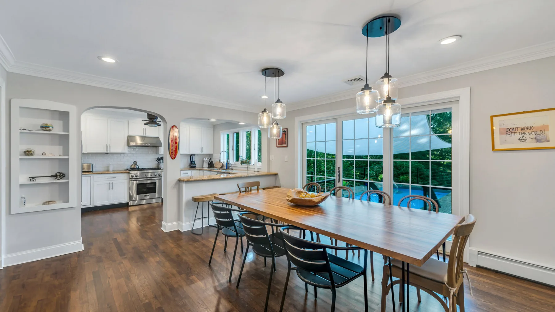A dining area with a long wooden table beside large windows.