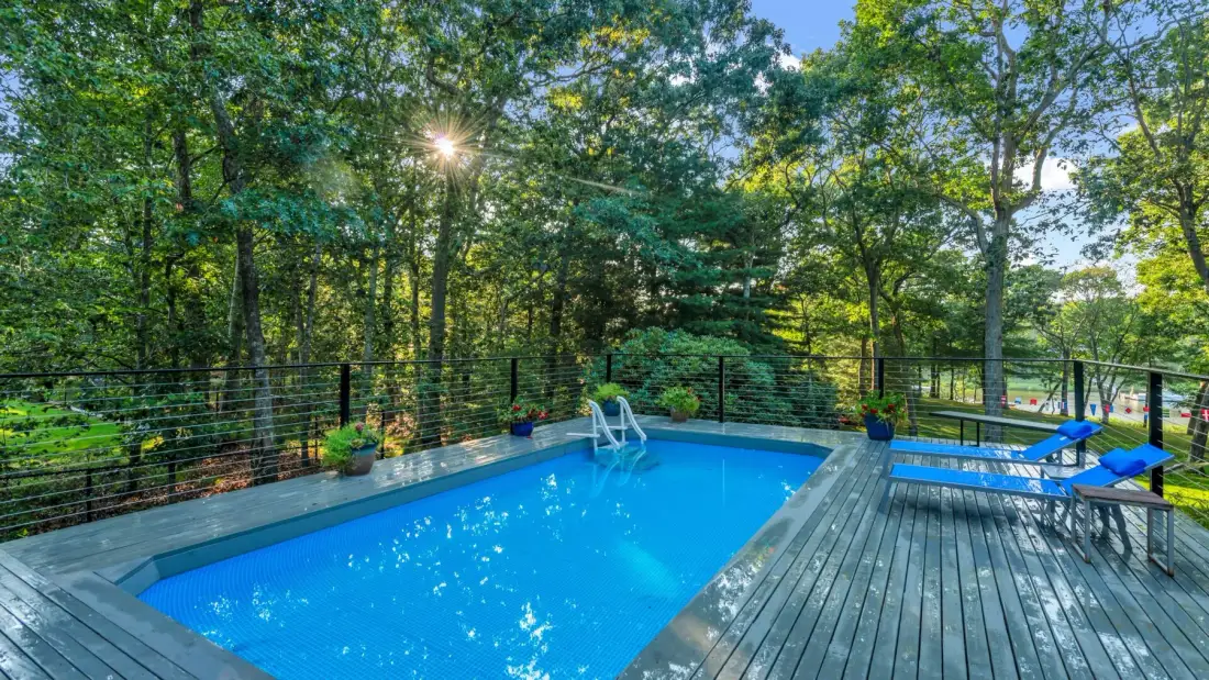 An outdoor swimming pool sits beside a wooden deck surrounded by trees.