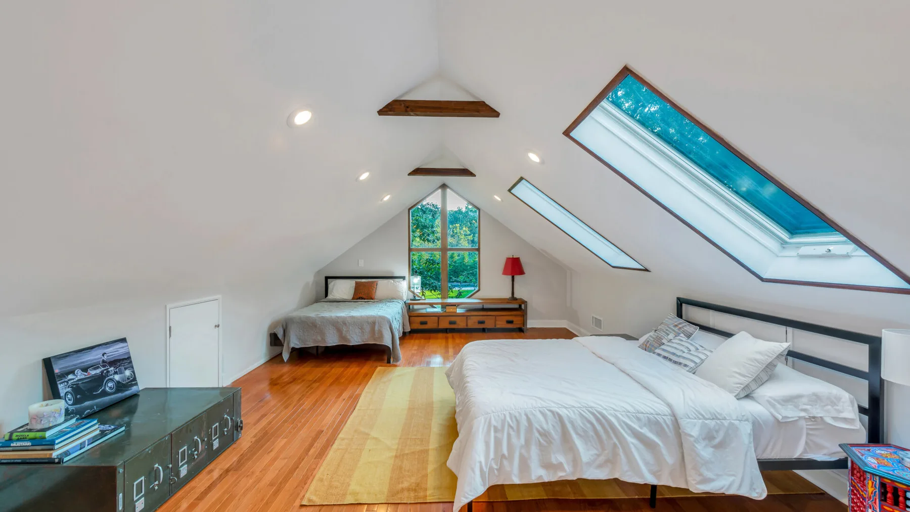 A bright attic bedroom with beds, a wooden floor, and slanted skylights.