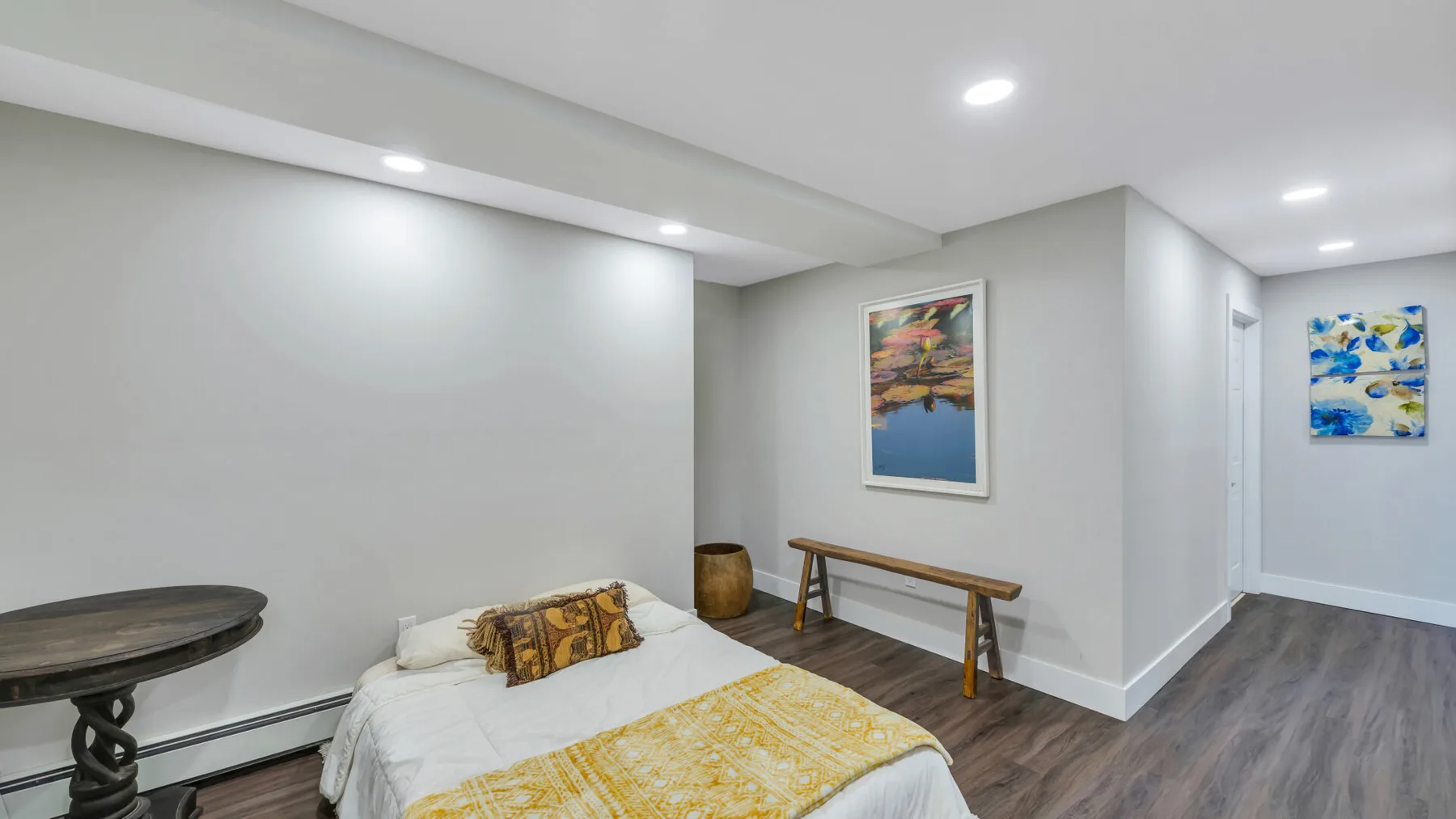 A bedroom with a bed, colorful artwork, and a wooden bench.