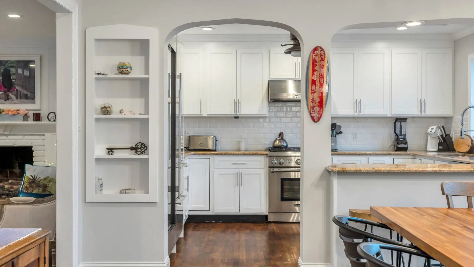 A bright kitchen with white cabinets, a central island, and a wooden dining table.