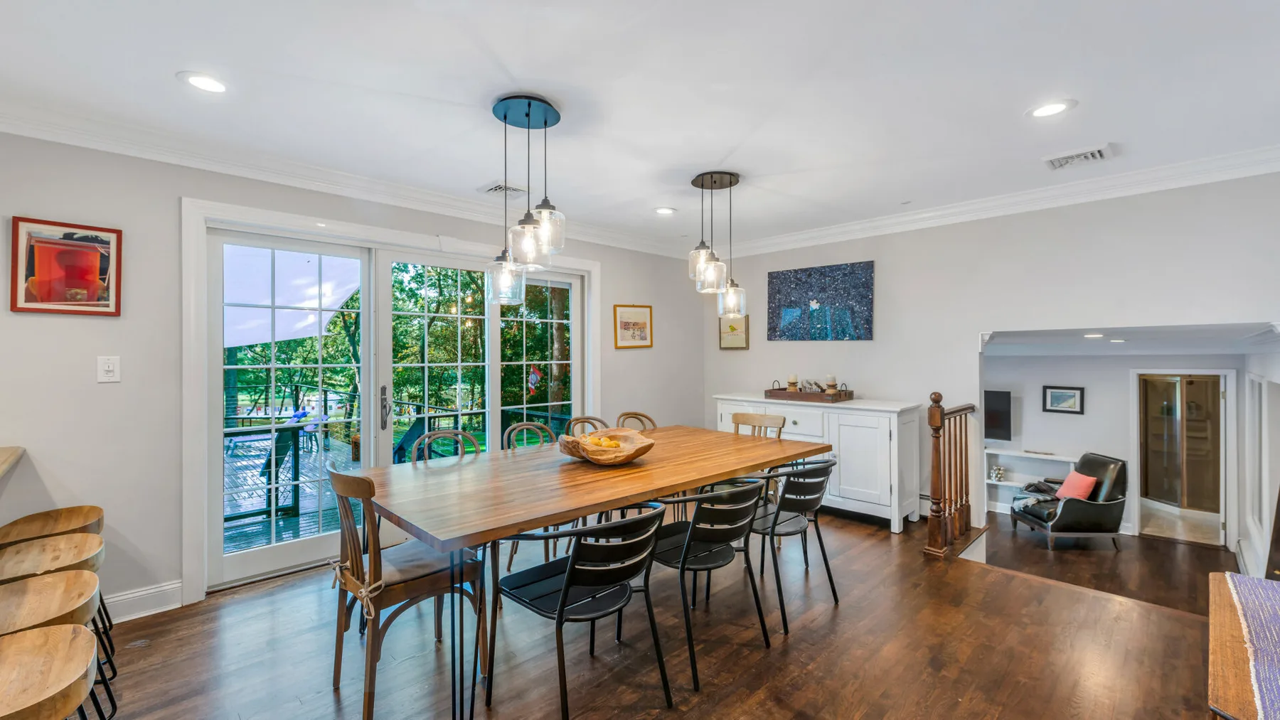 A dining area with a long wooden table and chairs beside large windows.