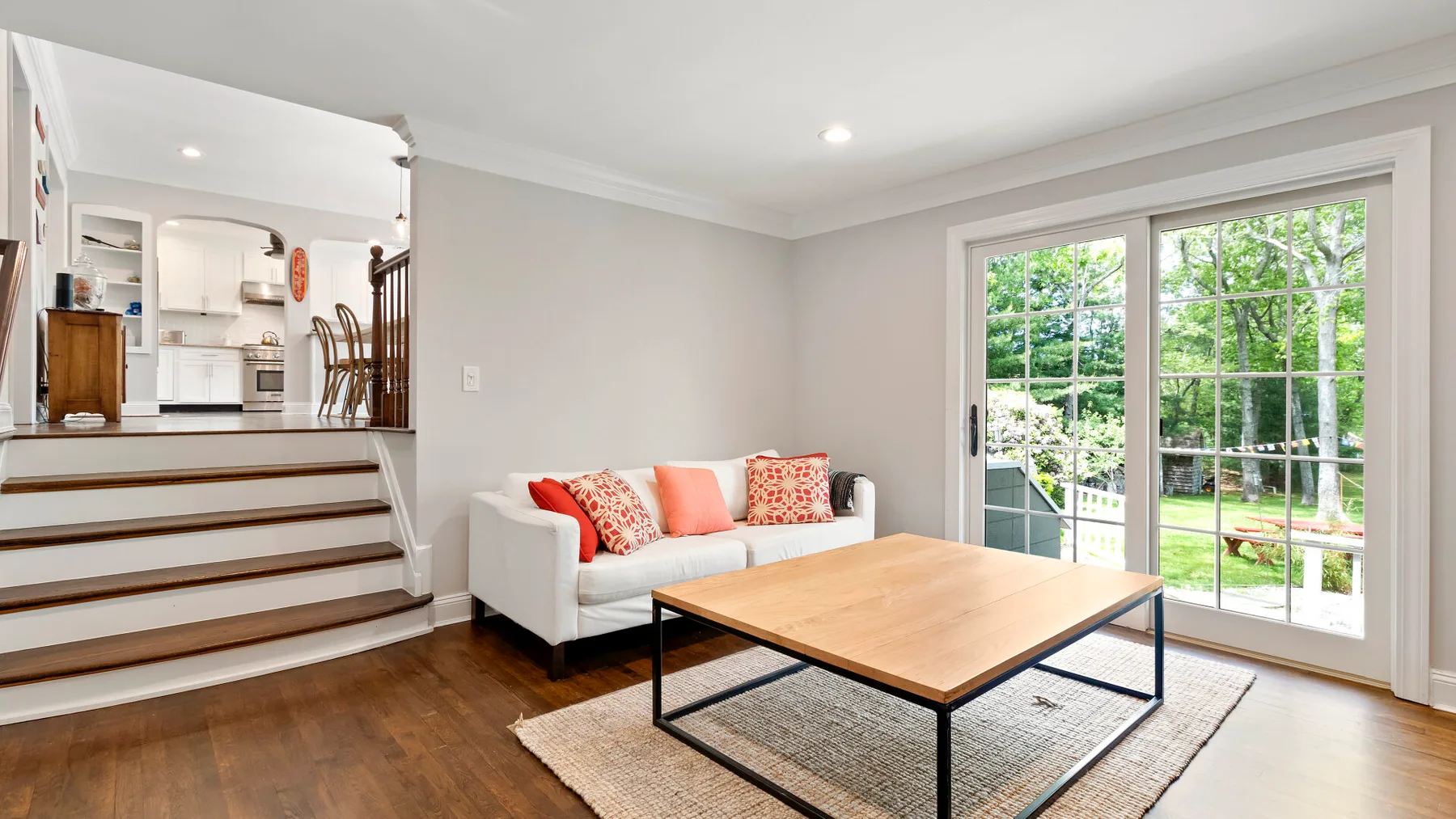A bright living room with a sofa, coffee table, and large windows overlooking greenery.