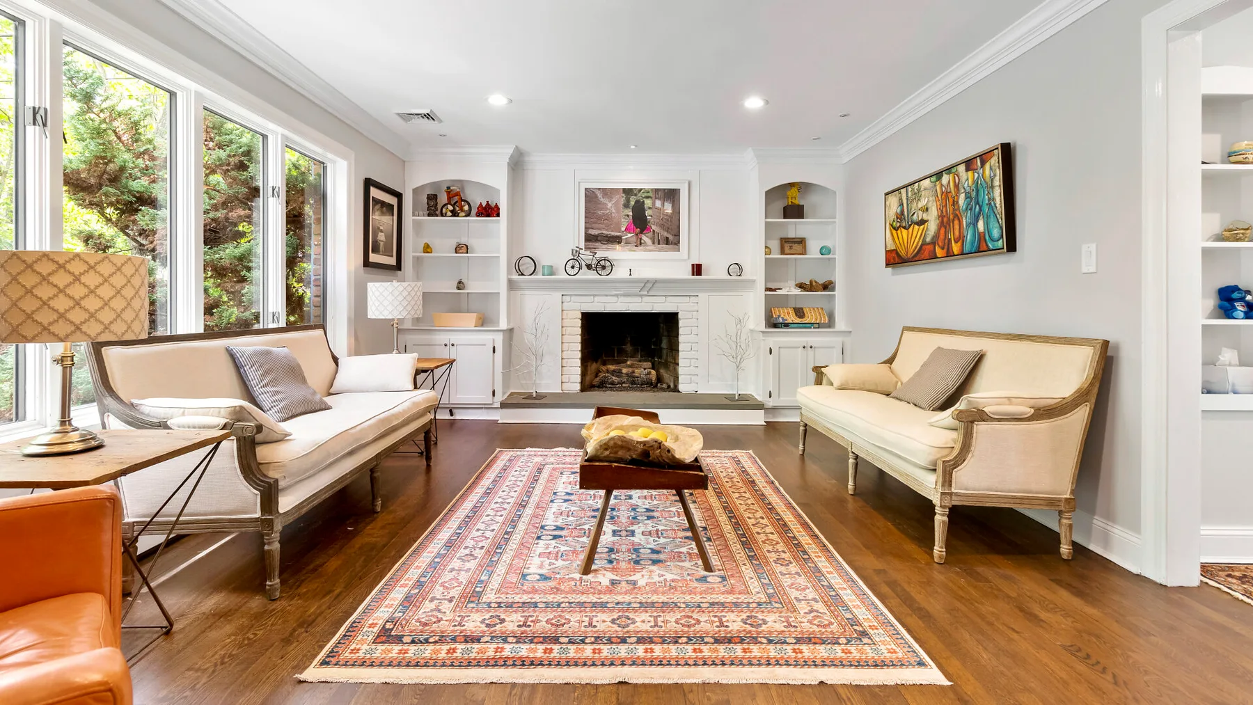 A bright living room with seating arranged around a patterned rug and fireplace.