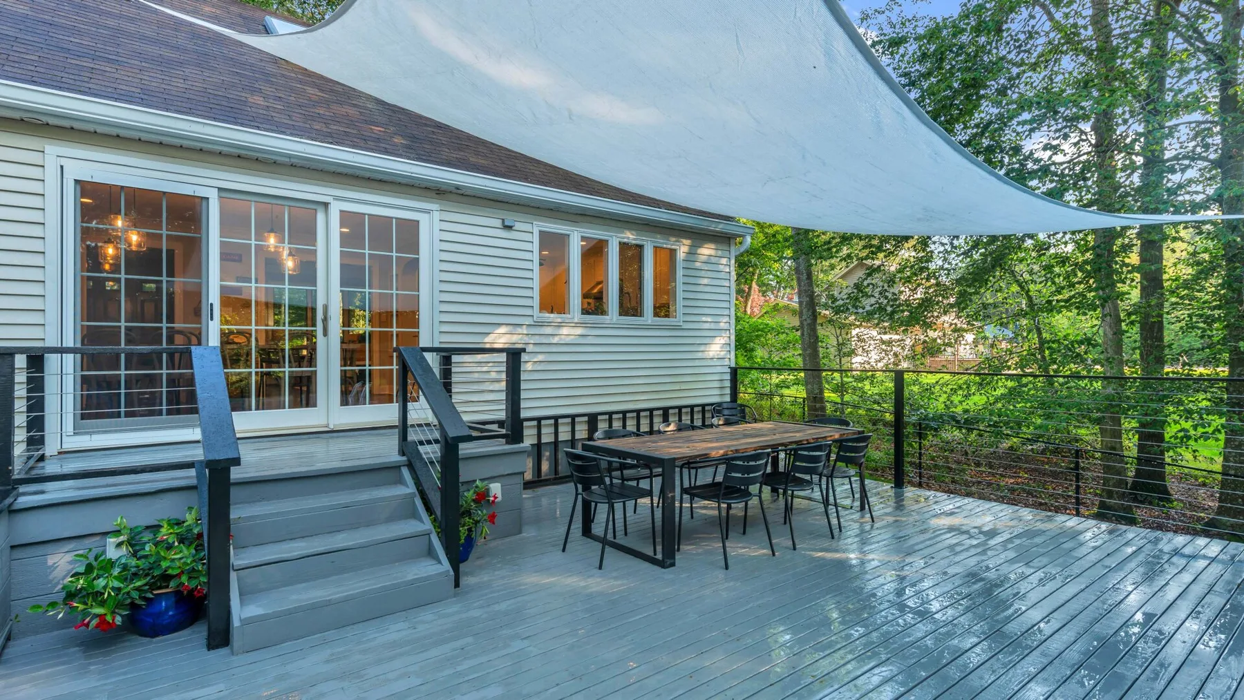 A raised outdoor deck with a dining table beside a house, shaded by a canopy.