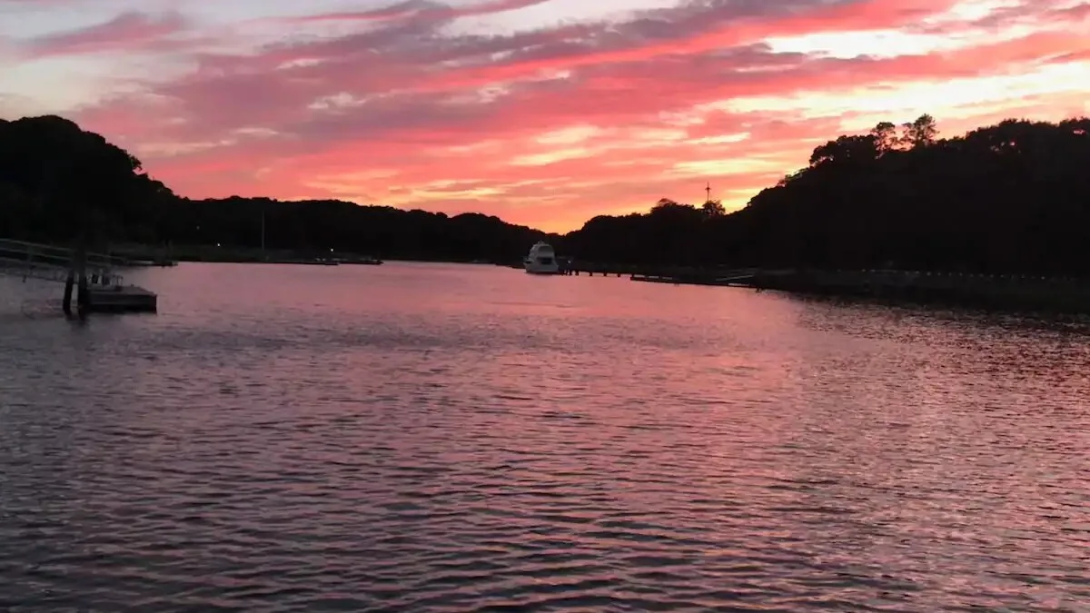 A calm stretch of water reflects a pink sunset between dark, wooded shores.