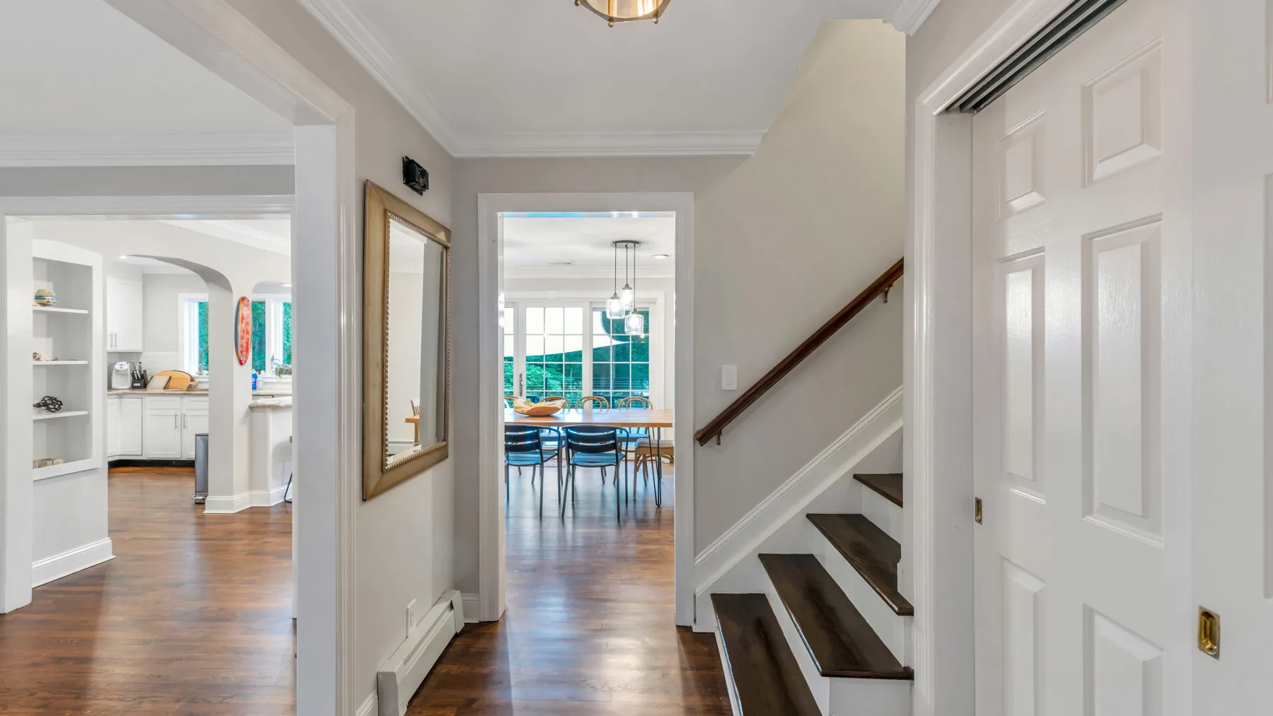 A bright hallway with a staircase and a dining area visible beyond.