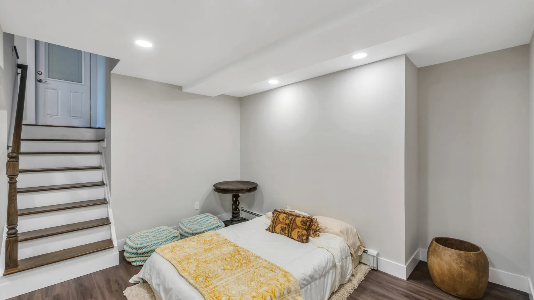 A bedroom with a bed, small table, and staircase.