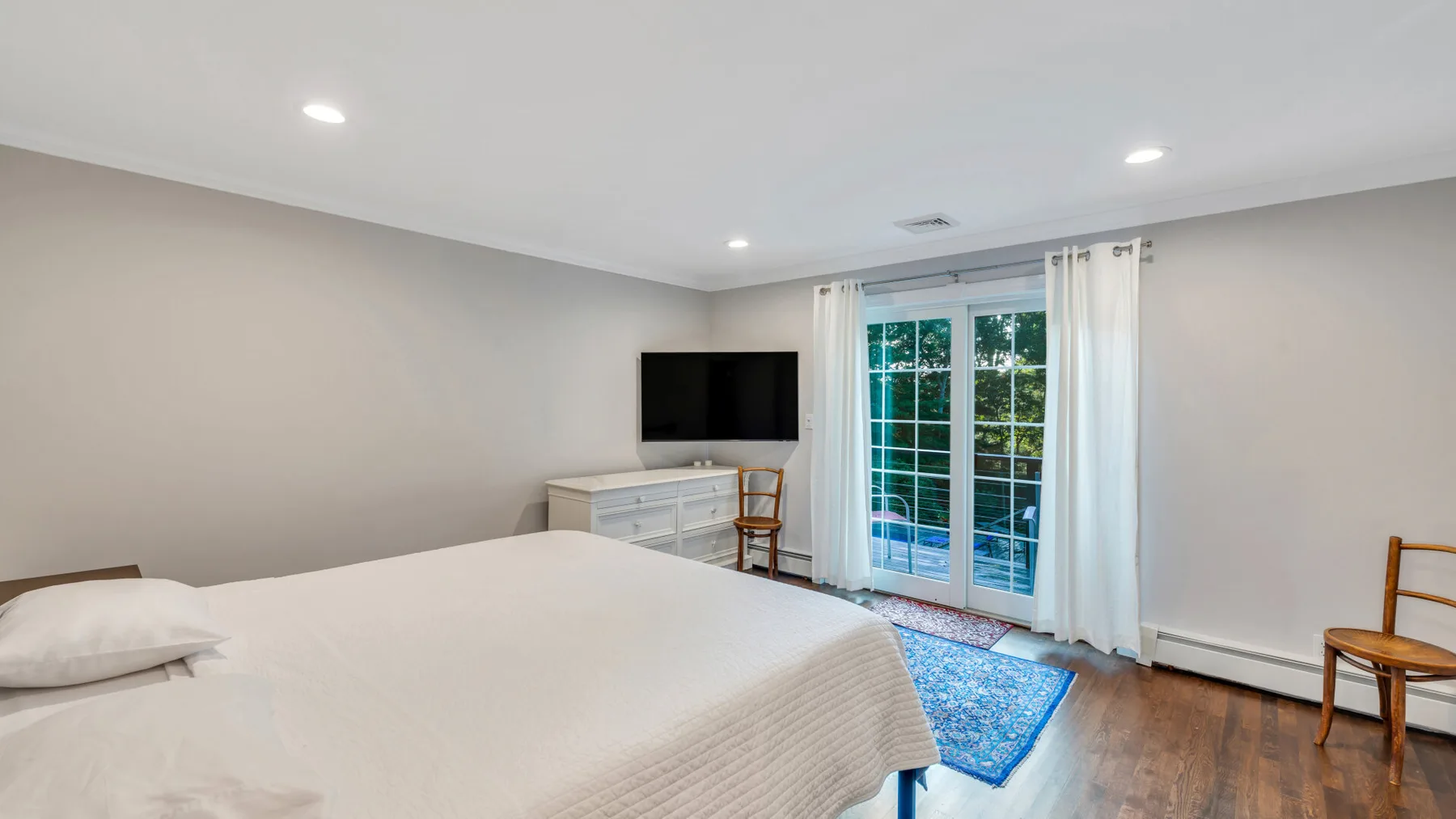 A bedroom with a bed, television, and glass doors opening to a balcony.
