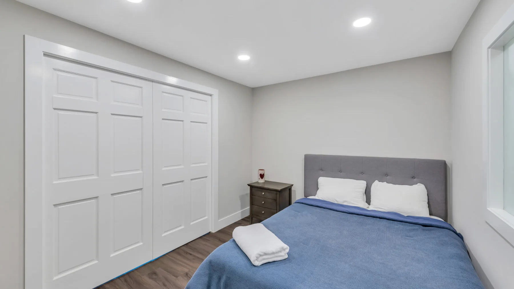 A bedroom with a bed, blue bedding, and white closet doors.
